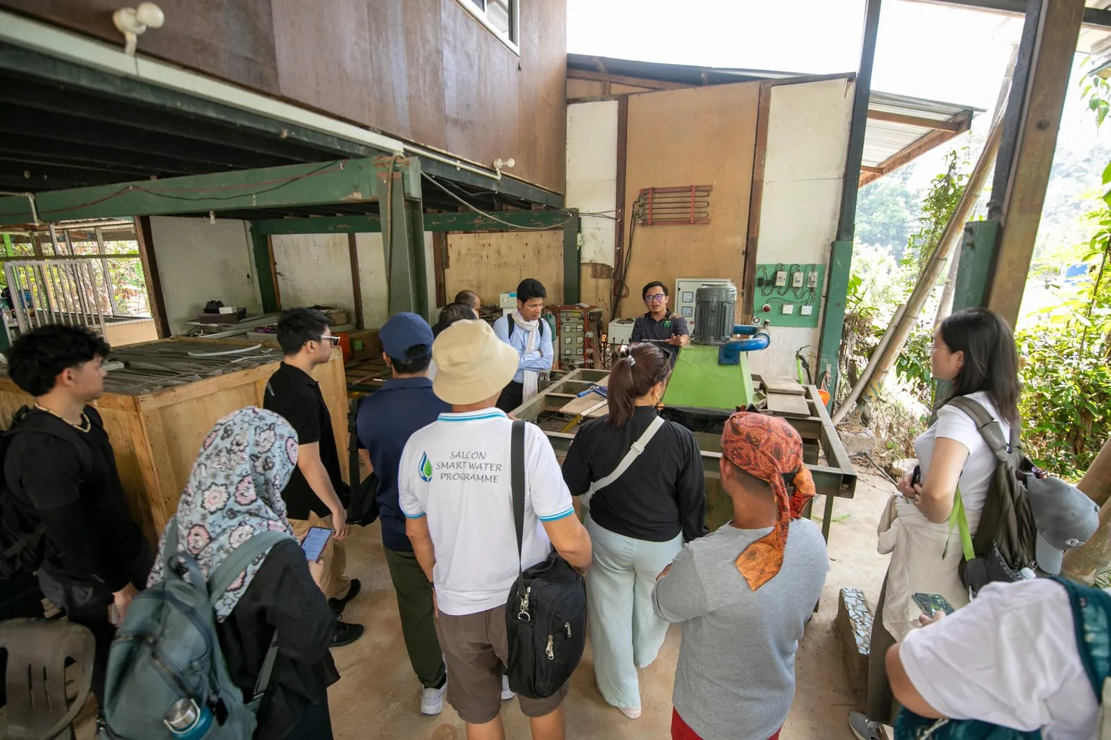 CANSEA members gathered around a micro hydro turbine bench at the TONIBUNG centre while a trainer explains the system