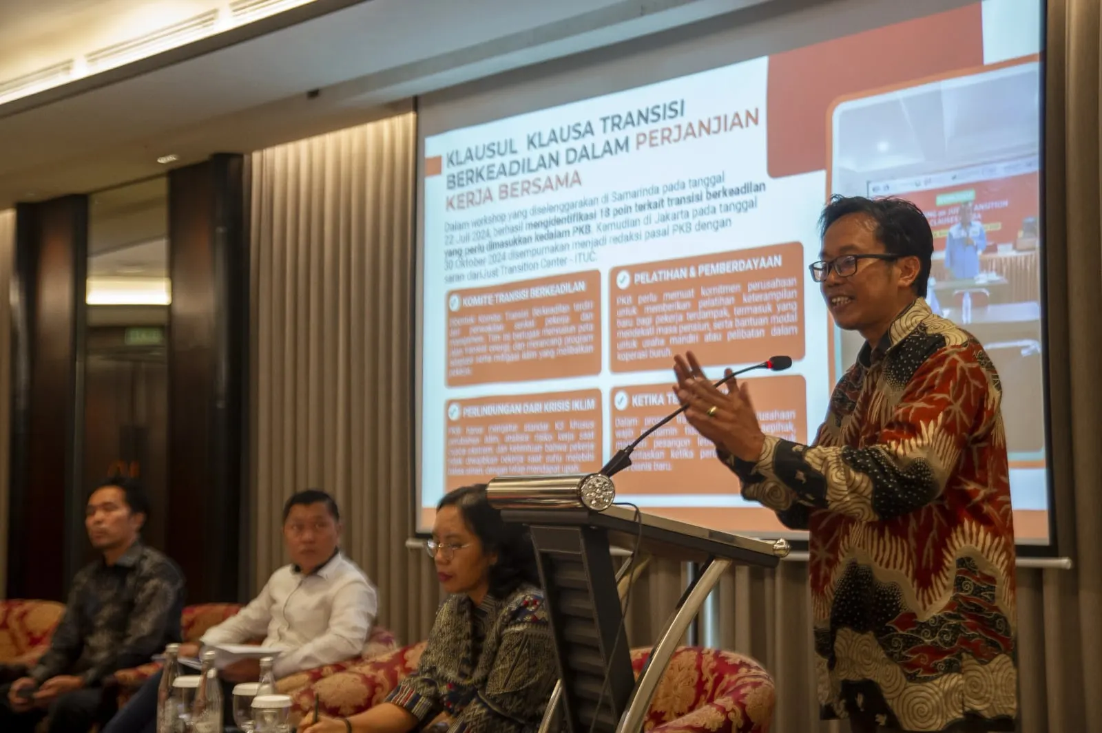 A speaker at a lectern beside a slide setting out just transition clauses in collective labour agreements