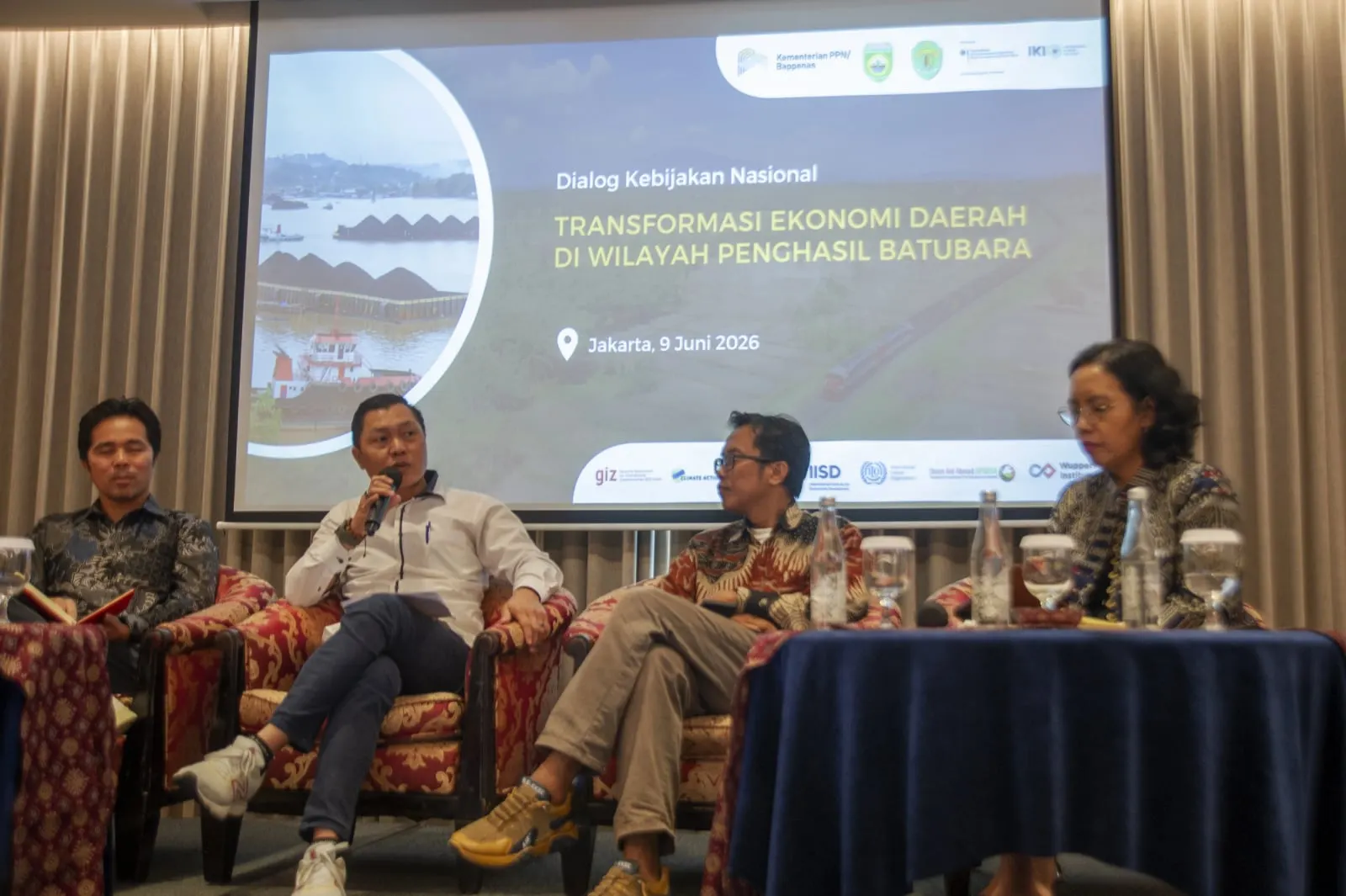 Four panellists seated beneath the dialogue's title slide, one of them speaking into a microphone