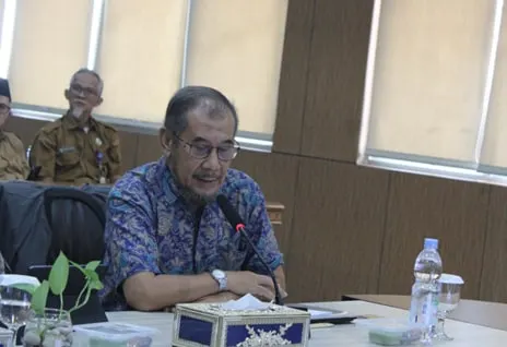 A man in a patterned batik shirt speaking into a table microphone