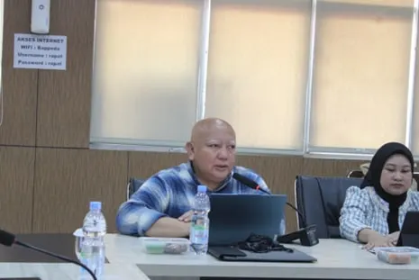 A man speaking beside an open laptop at the meeting table, a colleague seated to his right
