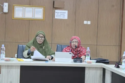 Two women seated together at the table, one holding papers and the other speaking into a microphone