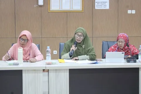 Three women seated at the table, the one in the centre speaking into a handheld microphone