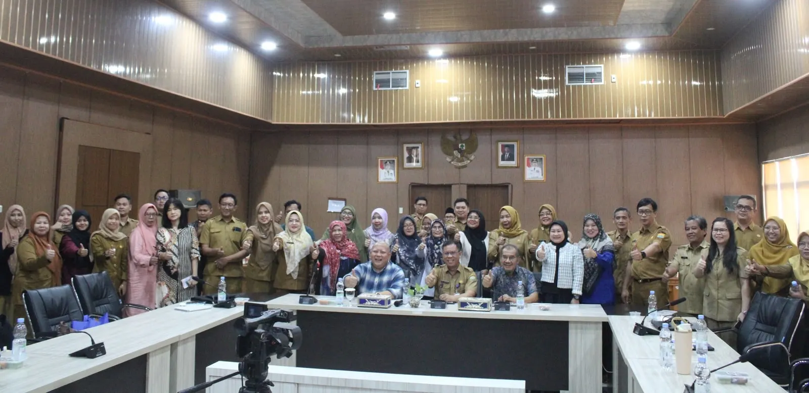 The full meeting gathered for a group photograph in the Bappeda South Sumatra chamber, standing behind the conference tables beneath the national emblem