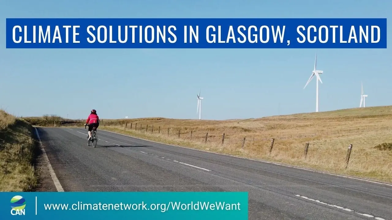 A cyclist on a rural road beside wind turbines, under the title “Climate solutions in Glasgow, Scotland”