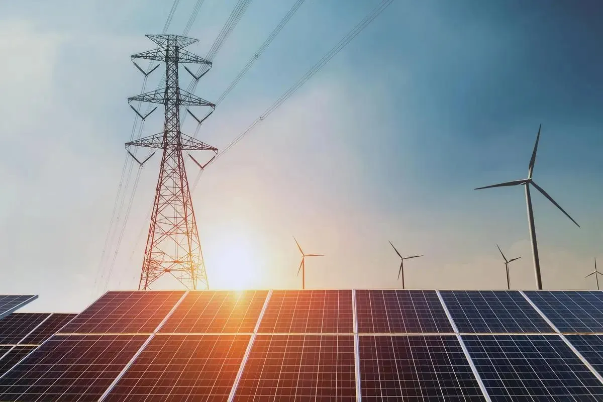 A transmission tower and wind turbines above rows of solar panels at sunset