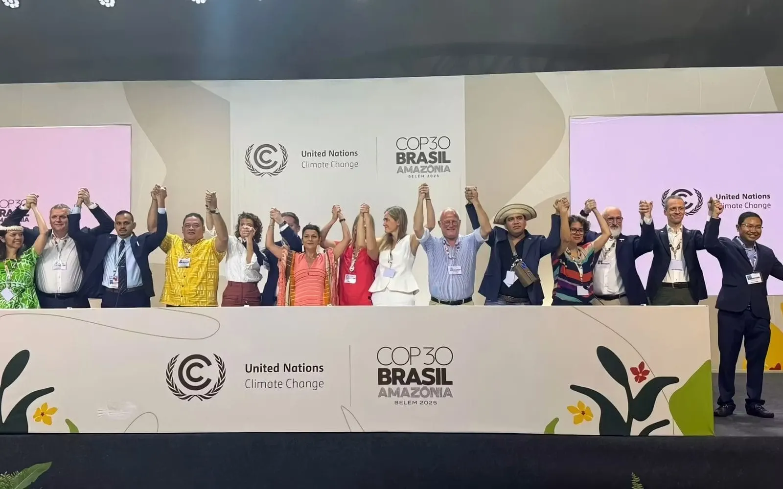 Civil-society representatives standing with hands raised and joined on stage at COP30 in Belem, Brazil
