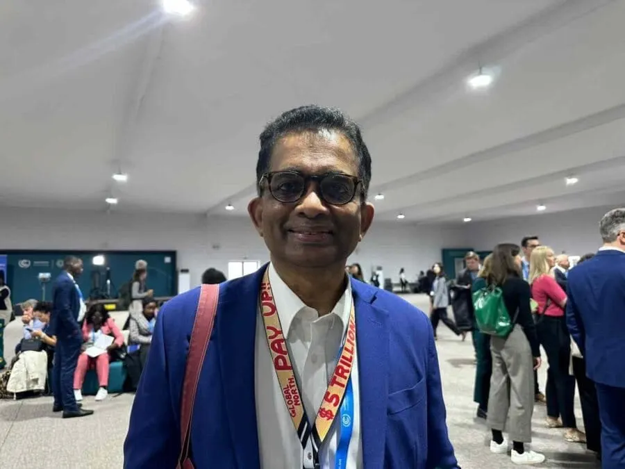 Nithi Nesadurai at COP29 in Baku, wearing a “Global North: pay up, $5 trillion” lanyard in a conference hall