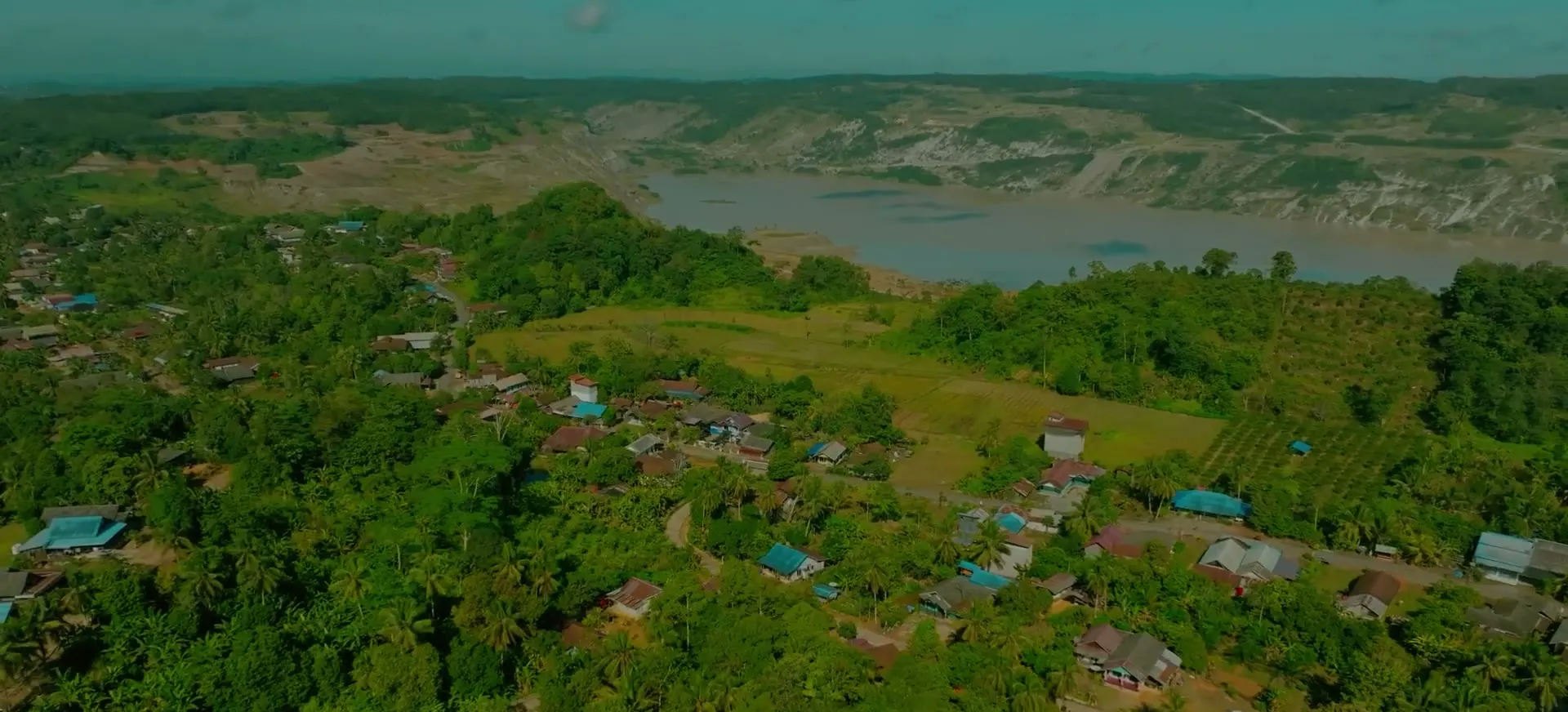 Aerial view of a village and forest in East Kalimantan beside the flooded pit of a former coal mine