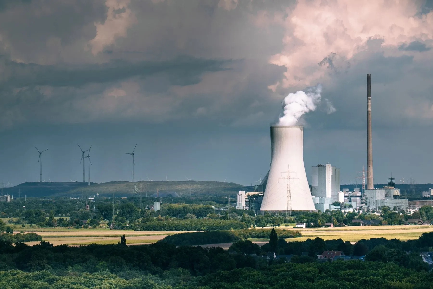 A coal power station beside wind turbines under a dramatic sky, showing the shift from coal toward renewable energy
