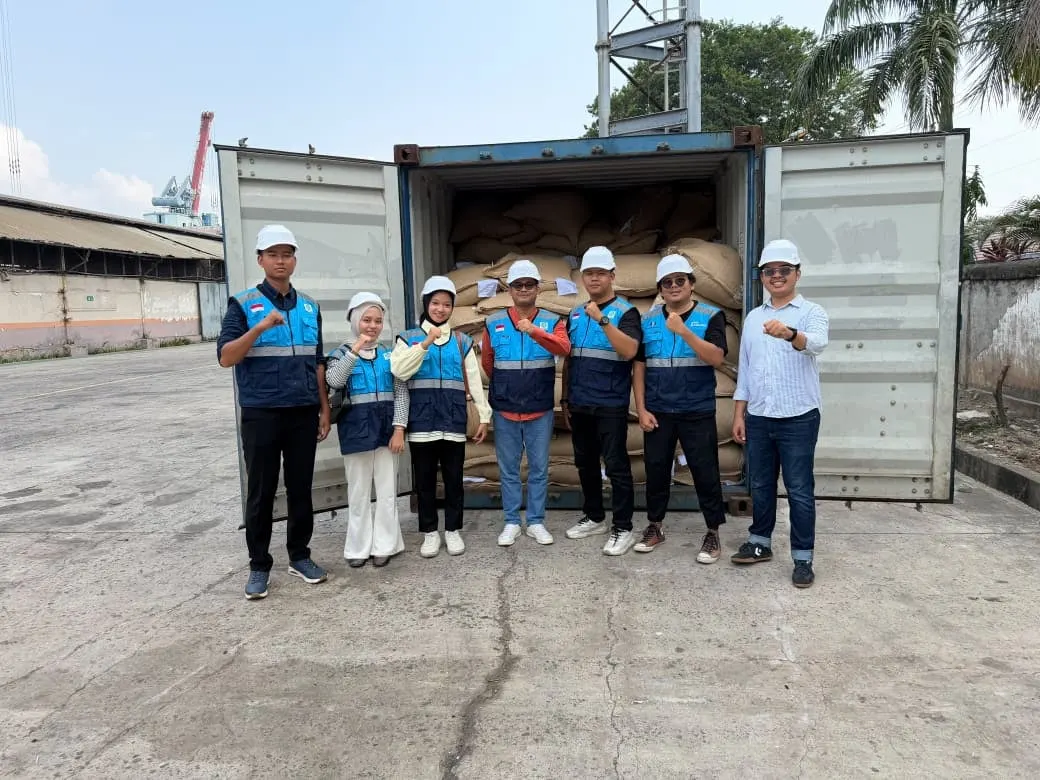 Robby and seven colleagues in hard hats and high-visibility vests standing in front of an open shipping container stacked with sacks of coffee beans