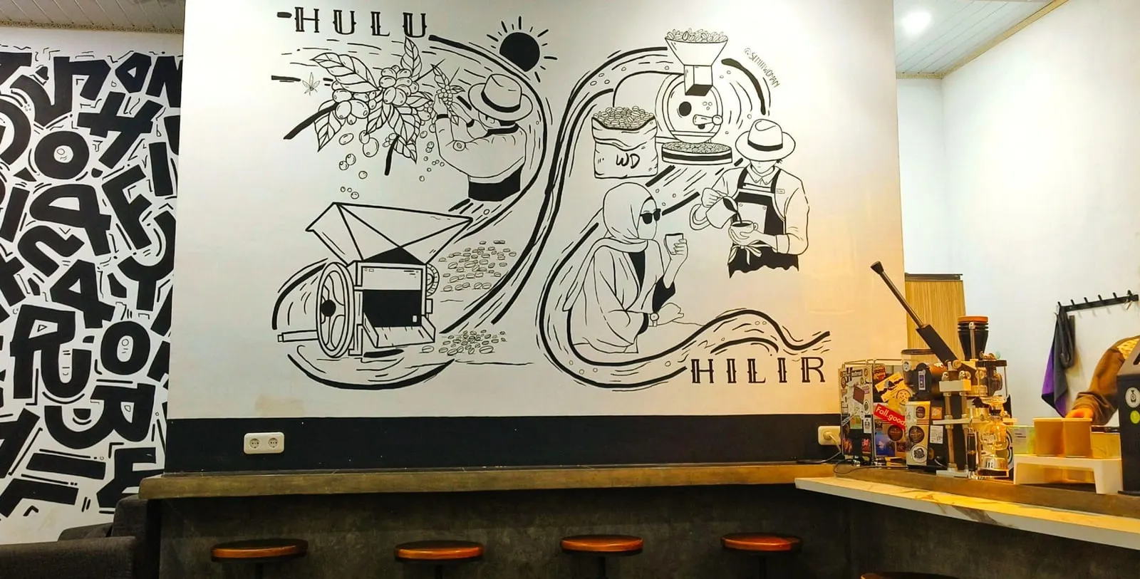 A hand-painted mural along the café wall: coffee cherries and a picker lettered HULU at one end, a roaster, a barista and a woman drinking lettered HILIR at the other, the two joined by a flowing line