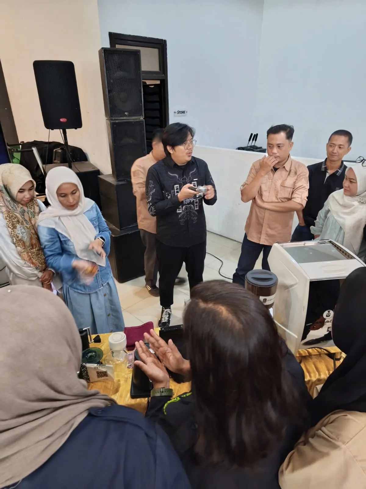 A group of workshop participants gathered closely around Robby as he holds a portafilter and explains coffee varieties