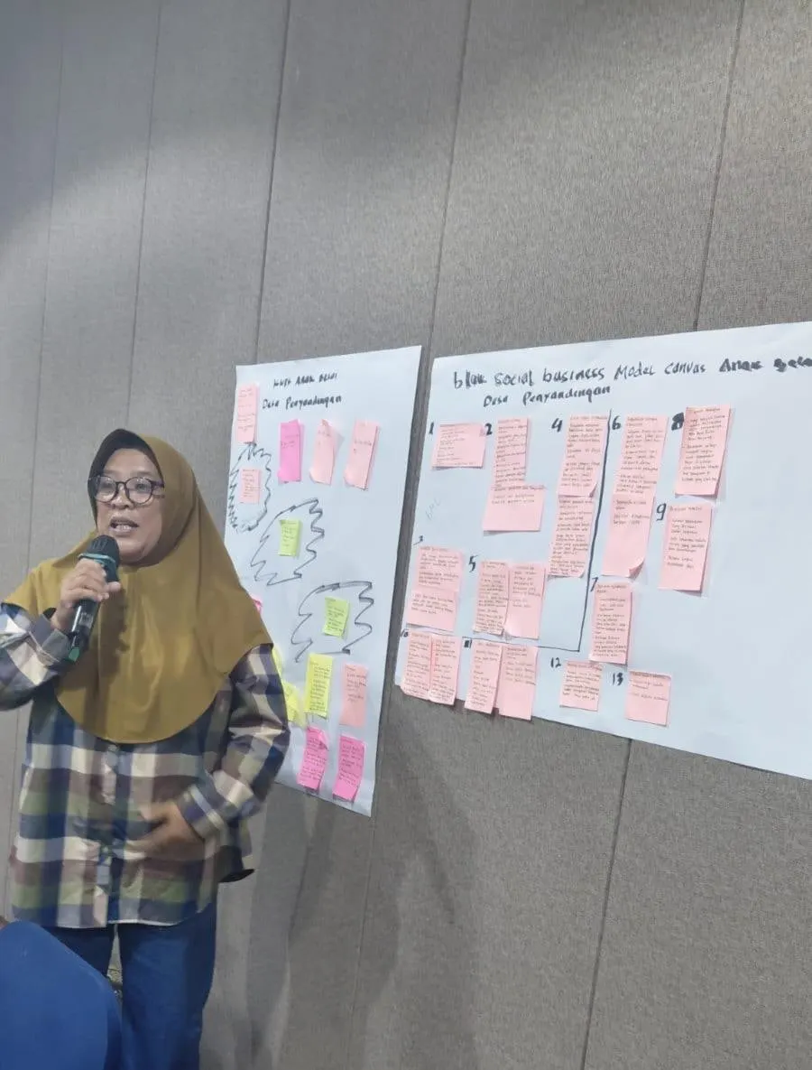 Ibu Ani speaking into a microphone beside two flipcharts covered in hand-written notes and sticky notes